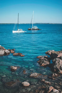 Sailboats sailing in sea against blue sky