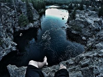 Man sitting at the edge of a cliff with stream below