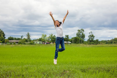 In an organic farmed rice field, happy asian children jumping raise their hands to the sky and grin.