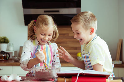 Cute sibling preparing food while reading recipe in book