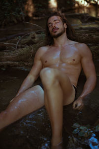 Shirtless young man sleeping by log in lake