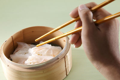 Close-up of hand having dim sum in container with chopsticks on table