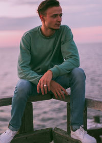 Full length of young man sitting against sea during sunset