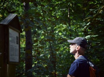 Side view of man wearing cap reading information sign in forest