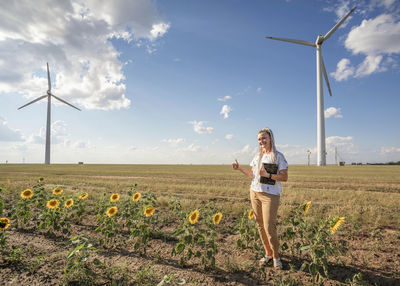 Smiling blogger girl with bright braids shoots story about green energy, wind energy, wind turbines