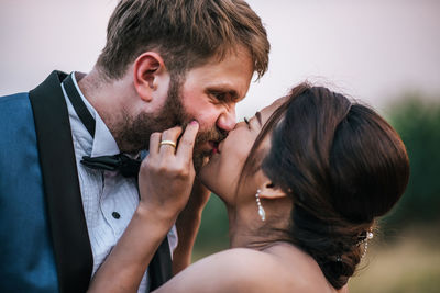 Newlywed couple kissing on field against sky