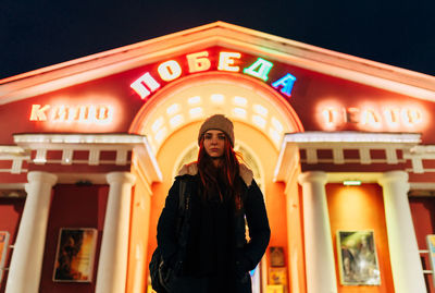 Portrait of smiling woman standing against illuminated building