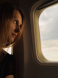 Traveling mood, young woman look at sunset sky in aircraft plane illuminator window