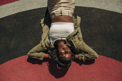 Carefree young woman with hands behind head relaxing in playground on sunny day