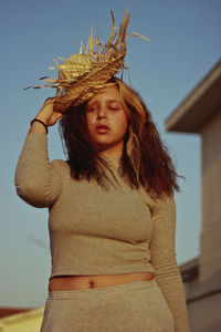 Young woman with wicker basket standing against sky