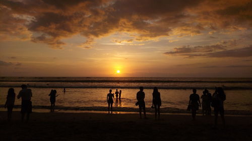 Silhouette people standing on beach against cloudy sky during sunset