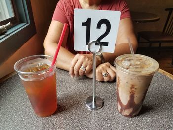 Midsection of woman having drinks with number 12 at table in cafe