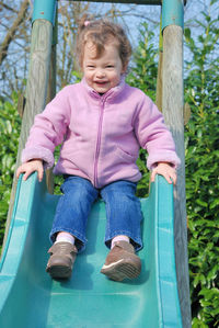 Portrait of cute girl sliding on slide in playground