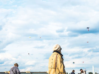 Rear view of people flying birds against sky