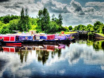 Boats moored in river against cloudy sky