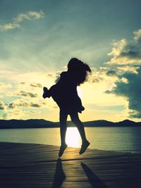 Silhouette girl standing by sea against sky during sunset