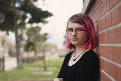 Portrait of teenage girl wearing eyeglasses by brick wall