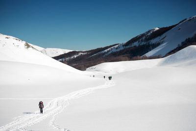 People walking on snowcapped mountain against clear sky