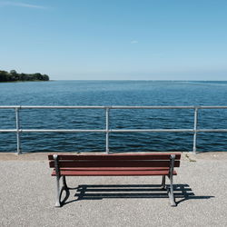 Empty bench by sea against clear sky