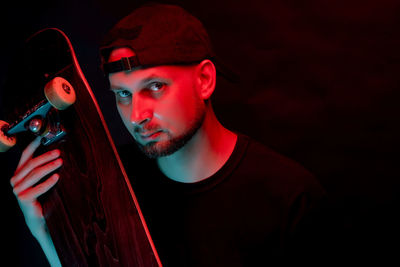 Portrait of man holding skateboard against black background