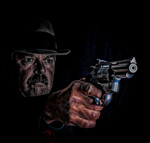 Senior man aiming gun standing against black background