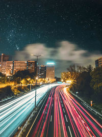 Light trails on street amidst buildings against sky at night