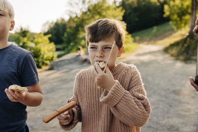 Boy wearing sweater and eating sausage with friend at summer camp