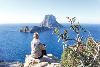 Rear view of woman sitting on rock against sea