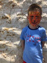 Cute boy with face paint standing against stone wall