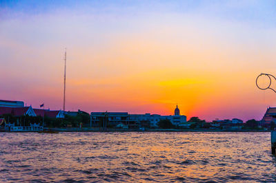 Buildings by sea against sky during sunset