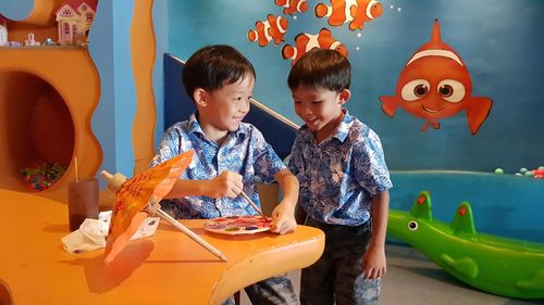 Brothers painting small umbrella at table