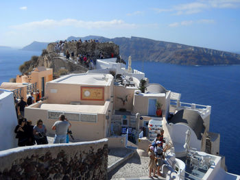 People looking at sea by buildings against sky