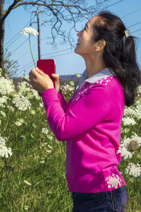 Side view of young woman using phone while standing on field