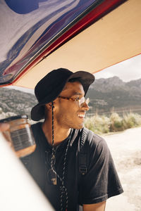 Smiling young man looking away while standing near van