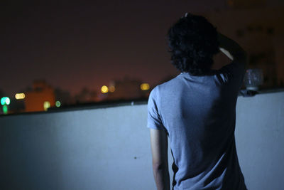 Rear view of woman standing against illuminated city at night