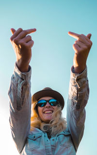 Woman in sunglasses showing obscene gesture against clear sky