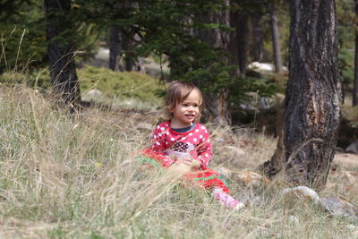 Cute smiling baby girl looking away while sitting in forest