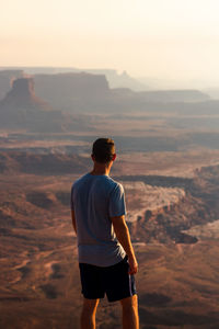 Rear view of man standing on mountain against sky during sunset