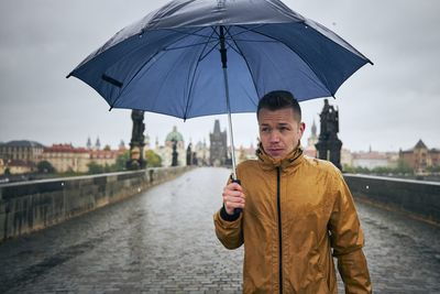 Man holding umbrella walking on bridge during rainy season