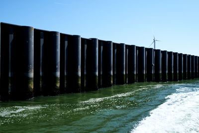 Wooden posts in sea against clear blue sky