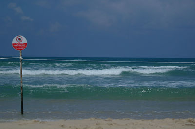 View of road sign by sea against sky