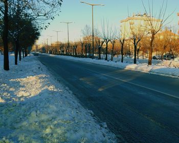 Road by bare trees against clear sky during winter