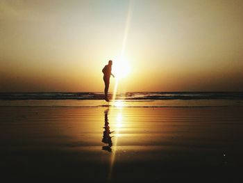 Silhouette man standing on beach against sky during sunset