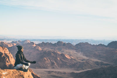 Man sitting on rock against sky