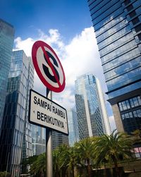 Low angle view of road sign against modern buildings in city