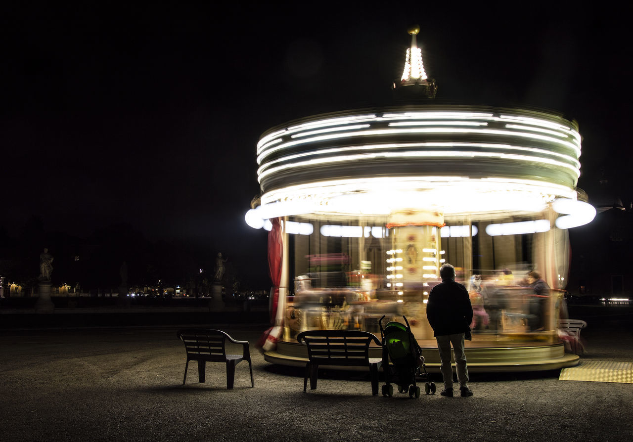 PEOPLE SITTING ON TABLE AT ILLUMINATED BUILDING