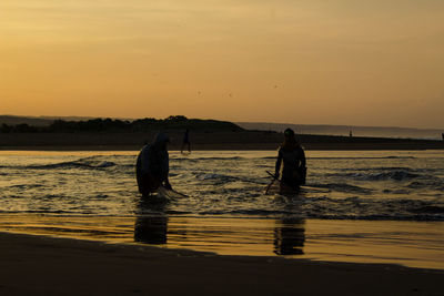 Silhouette people on beach against sky during sunset