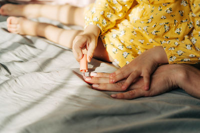 A little unrecognizable daughter paints her mother's nails with polish, playing like in a salon.