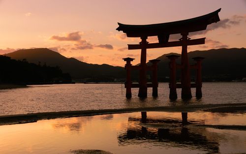 Gazebo by lake against sky during sunset