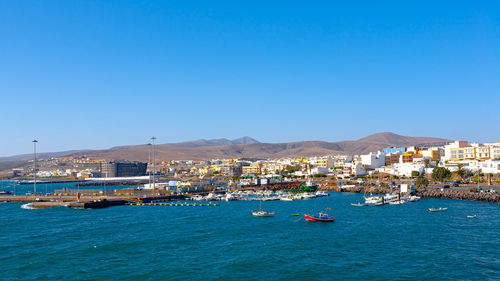 Sailboats in sea by city against clear blue sky